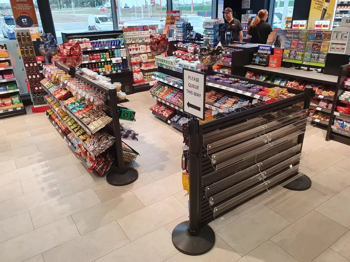 Store interior with snack displays and queue barriers directing customers toward the checkout area. 