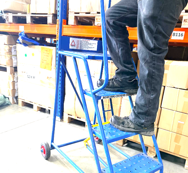 Worker using warehouse steps to safely access goods stored on warehouse racking.