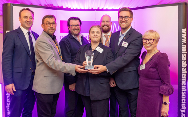 Group of professionals holding an award at a Quiet Mark certification event, representing the recognition of Quiet Mark certified products for reducing noise.
