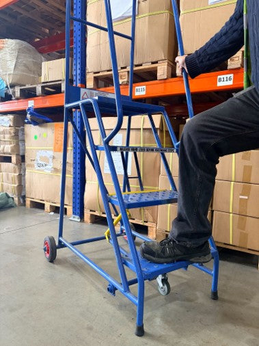 Warehouse worker using mobile safety steps to safely access stock stored on elevated warehouse shelving.