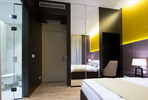 A modern hotel room interior featuring a made bed, mirrored wardrobes, and wood flooring, highlighting the type of space that benefits from furniture castors.