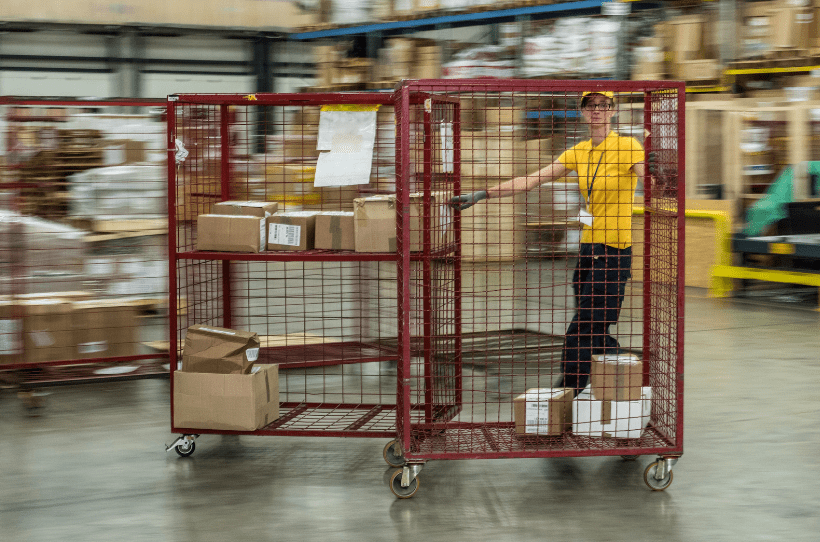 A supermarket stock worker operating a trolley roll cage using safe manual handling.