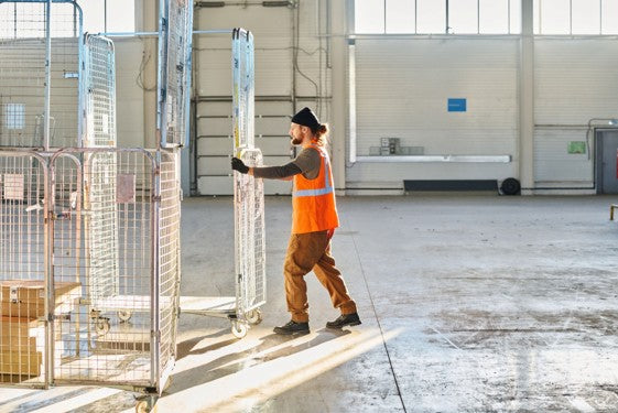 Warehouse worker moving supermarket cages designed for safe and efficient handling of goods.