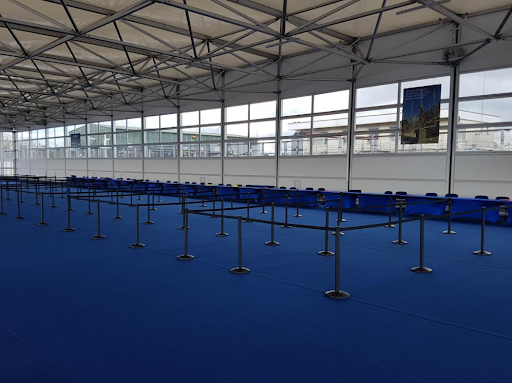 Large event hall with blue carpeting and several rows of black retractable belt stanchions used for organizing queue lines and crowd control.